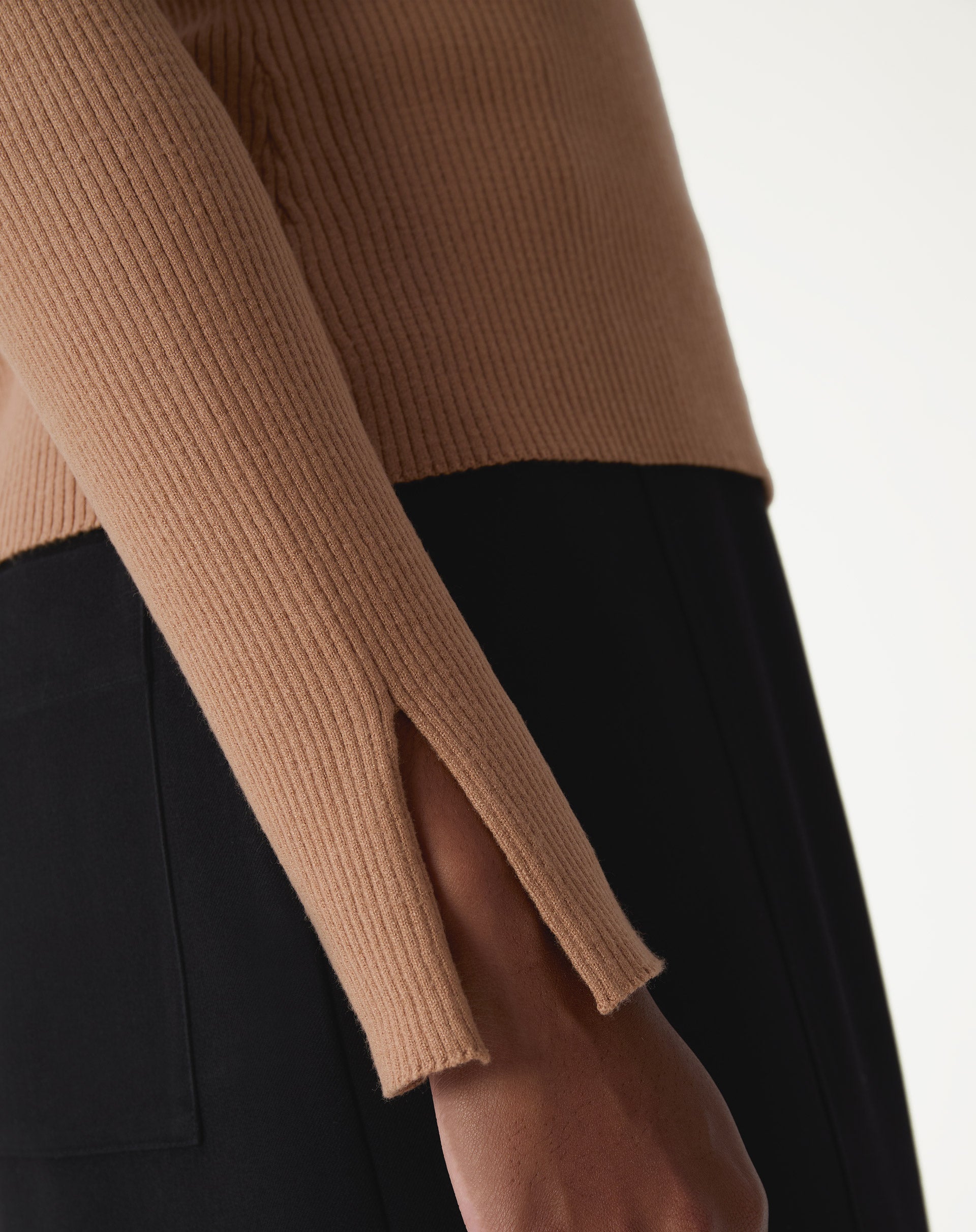 Detalhe do decote do suéter de tricô bege, mostrando o acabamento da gola redonda e a textura canelada.