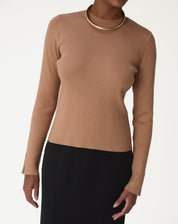 Mulher vestindo suéter de tricô bege com gola careca, combinado com saia preta — estilo minimalista e elegante.