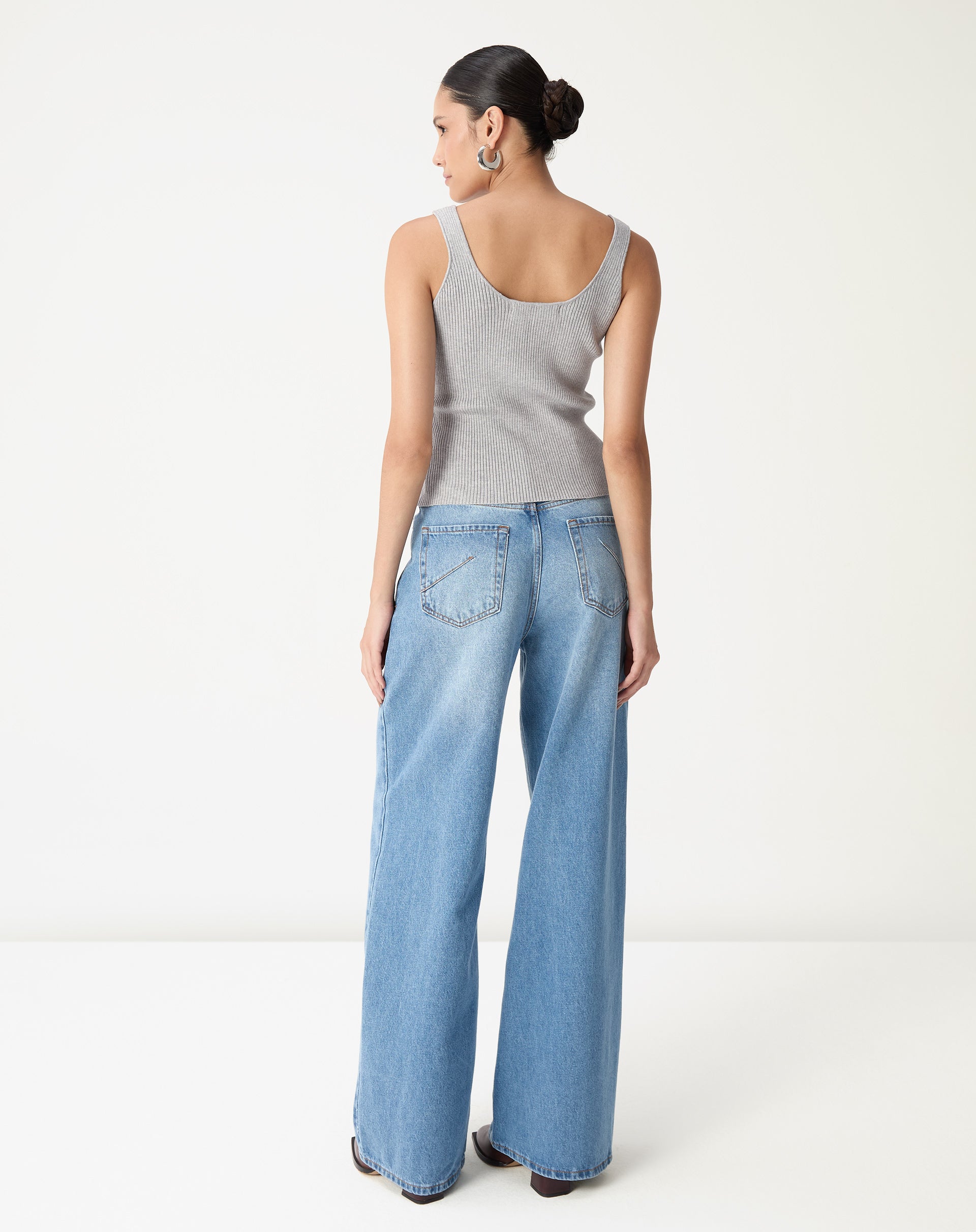 Vista traseira da regata tricot cinza mescla em modelo mostrando decote nas costas e comprimento até o quadril