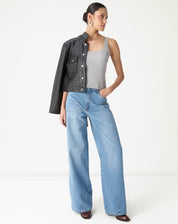 Look completo com regata tricot cinza mescla, calça jeans wide leg lavagem clara e jaqueta preta sobre o ombro