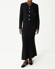 Vista frontal em corpo inteiro do conjunto cardigan e saia midi em tricot preto com sapatos baixos