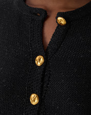 Close-up dos botões dourados texturizados no decote redondo do cardigan tricot preto
