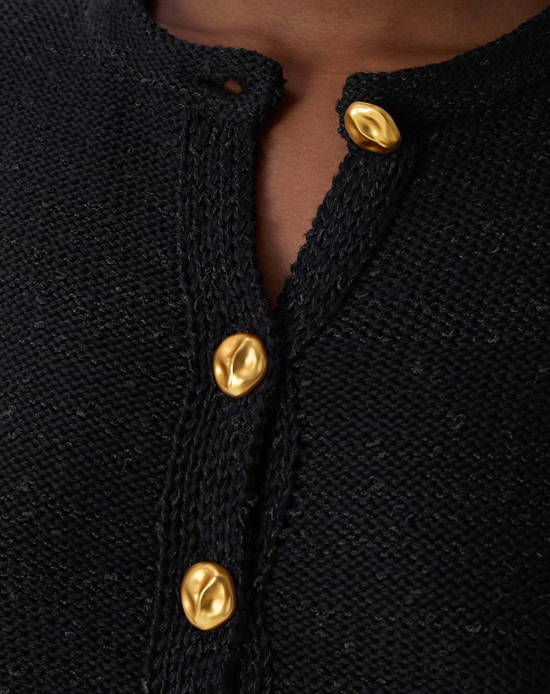 Close-up dos botões dourados texturizados no decote redondo do cardigan tricot preto