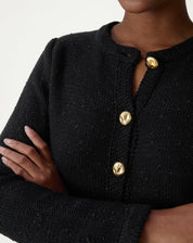 Detalhe do decote gola clássica e malha tricot preta com botão dourado visível