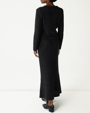 Vista traseira da saia longa tricot preta em modelo, mostrando o caimento alongado e a leve abertura na barra ao andar