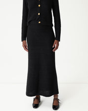 Visão frontal próxima da saia longa tricot preta destacando o ajuste na cintura e o caimento reto com leve evasê na barra