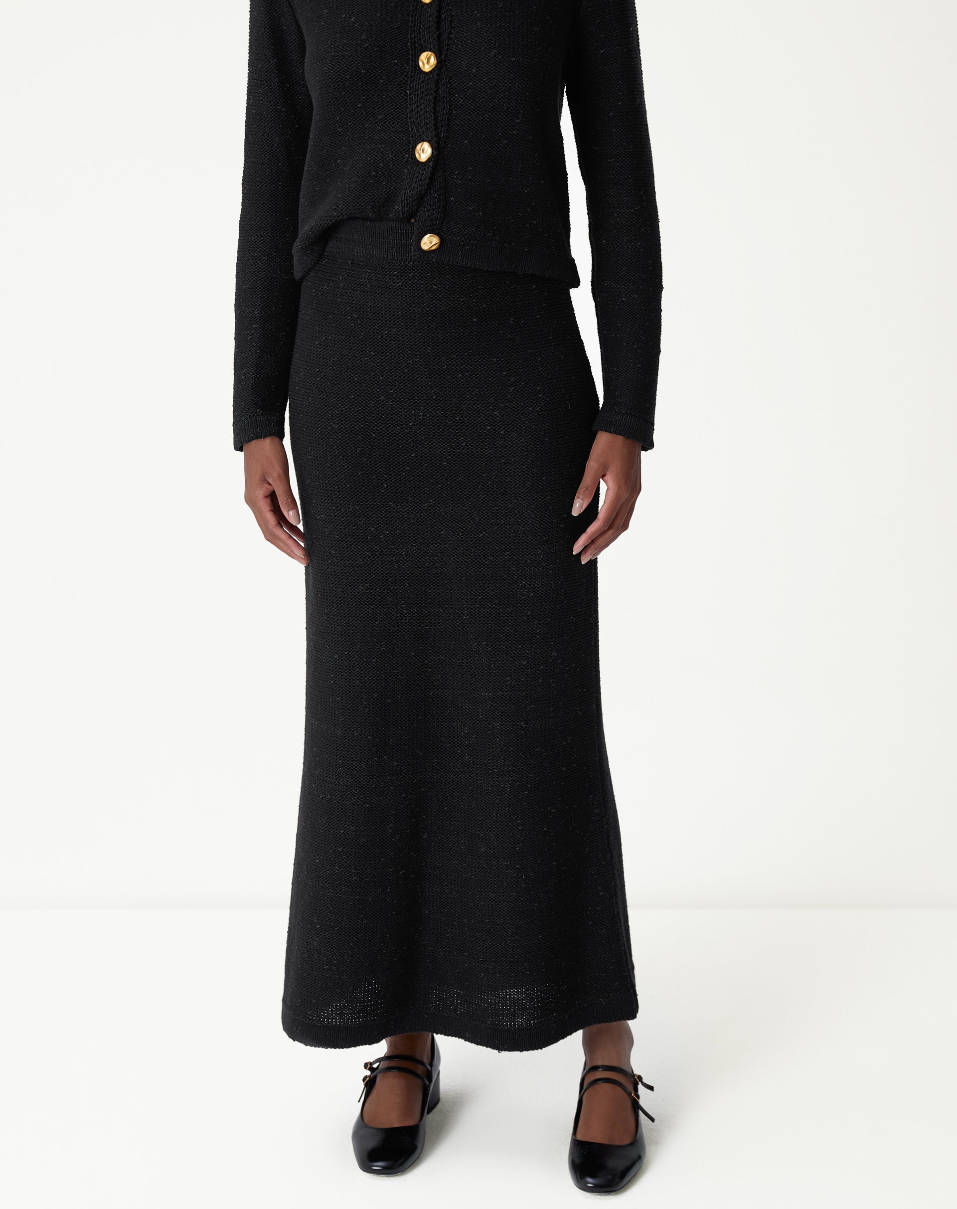 Visão frontal próxima da saia longa tricot preta destacando o ajuste na cintura e o caimento reto com leve evasê na barra