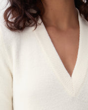 Rear view of the off-white midi knit dress on model, highlighting central slash at the hem and elongated fit; visible black boot