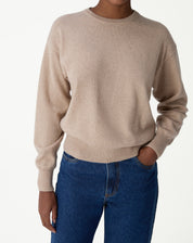 Suéter de gola careca em cashmere cor cáqui visto de frente, com estilo folgado e barra canelada, combinado com jeans azul.