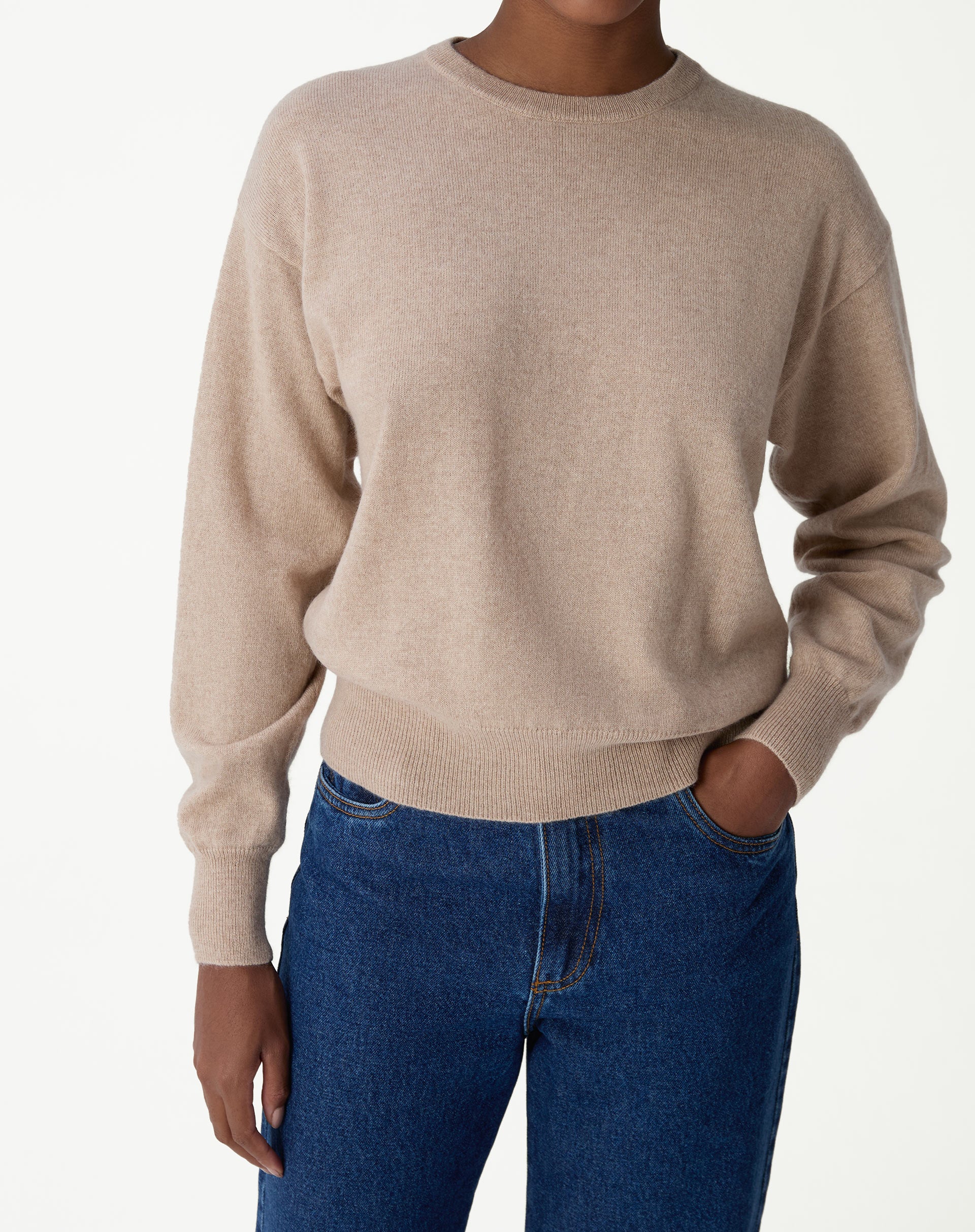 Suéter de gola careca em cashmere cor cáqui visto de frente, com estilo folgado e barra canelada, combinado com jeans azul.