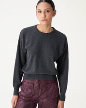 Modelo frontal usando suéter gola careca de cashmere cinza mescla escuro com calça vinho e botas pretas, visual completo do look