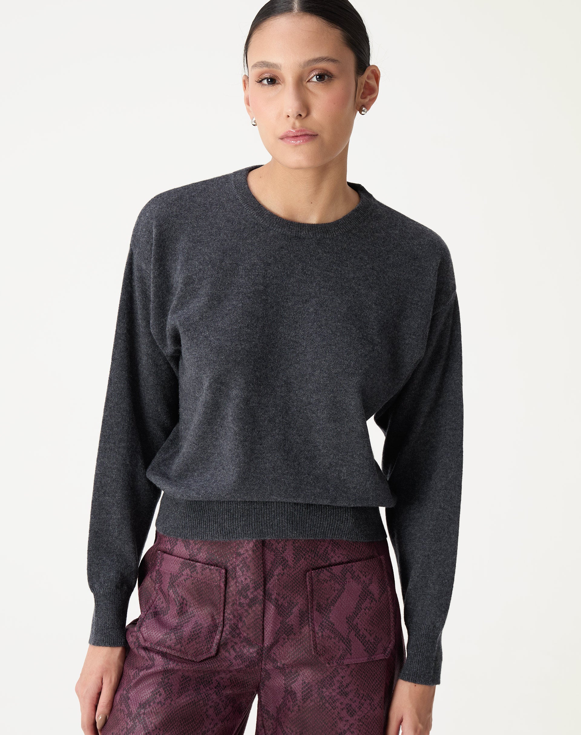 Modelo frontal usando suéter gola careca de cashmere cinza mescla escuro com calça vinho e botas pretas, visual completo do look