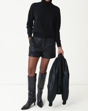 Mulher vestindo suéter gola alta de cashmere preto com shorts de couro e botas cano alto, look completo frontal