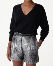 Modelo usando suéter de cashmere preto gola V com caimento loose e manga longa, combinado com shorts metálicos prateados e cinto - look elegante e despojado