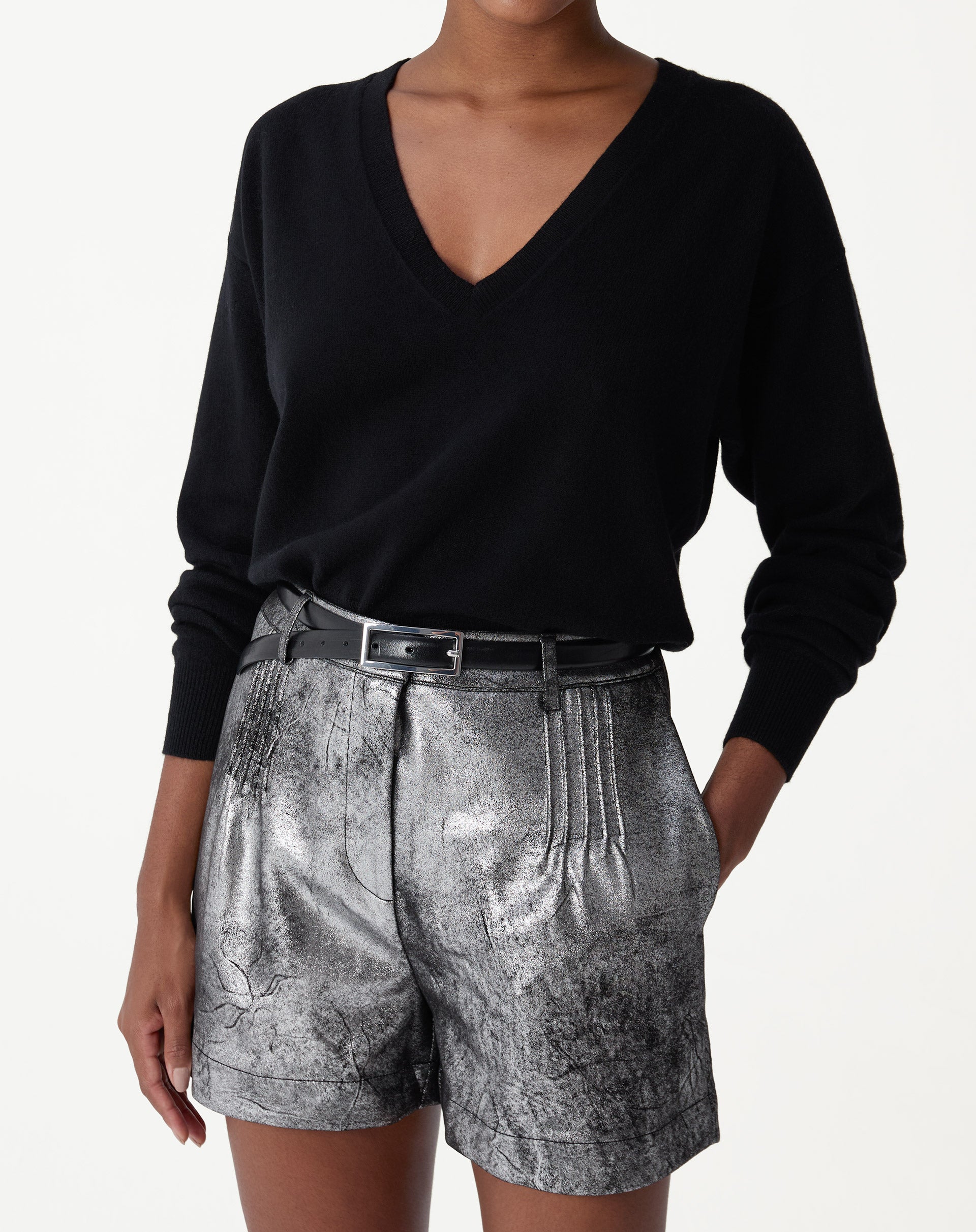 Modelo usando suéter de cashmere preto gola V com caimento loose e manga longa, combinado com shorts metálicos prateados e cinto - look elegante e despojado