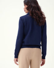 Detalhe lateral do suéter azul marinho com foco no punho canelado, textura de tricô e acabamento da barra junto à calça bege.