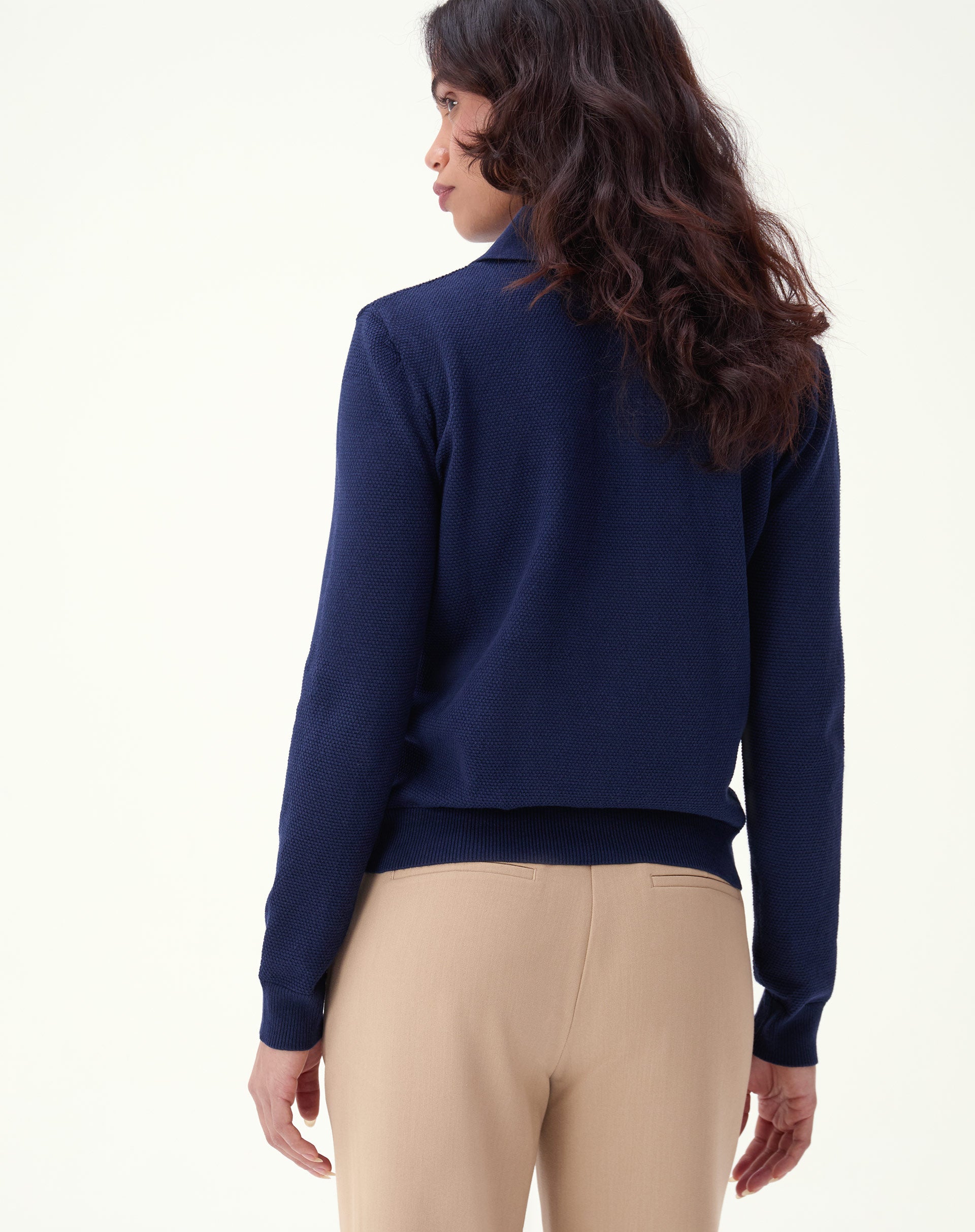 Detalhe lateral do suéter azul marinho com foco no punho canelado, textura de tricô e acabamento da barra junto à calça bege.