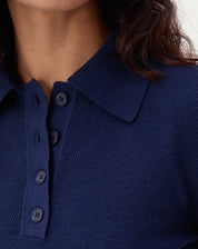 Vista traseira do suéter gola polo de tricô azul marinho mostrando barra canelada e caimento até o quadril, detalhe das costas.