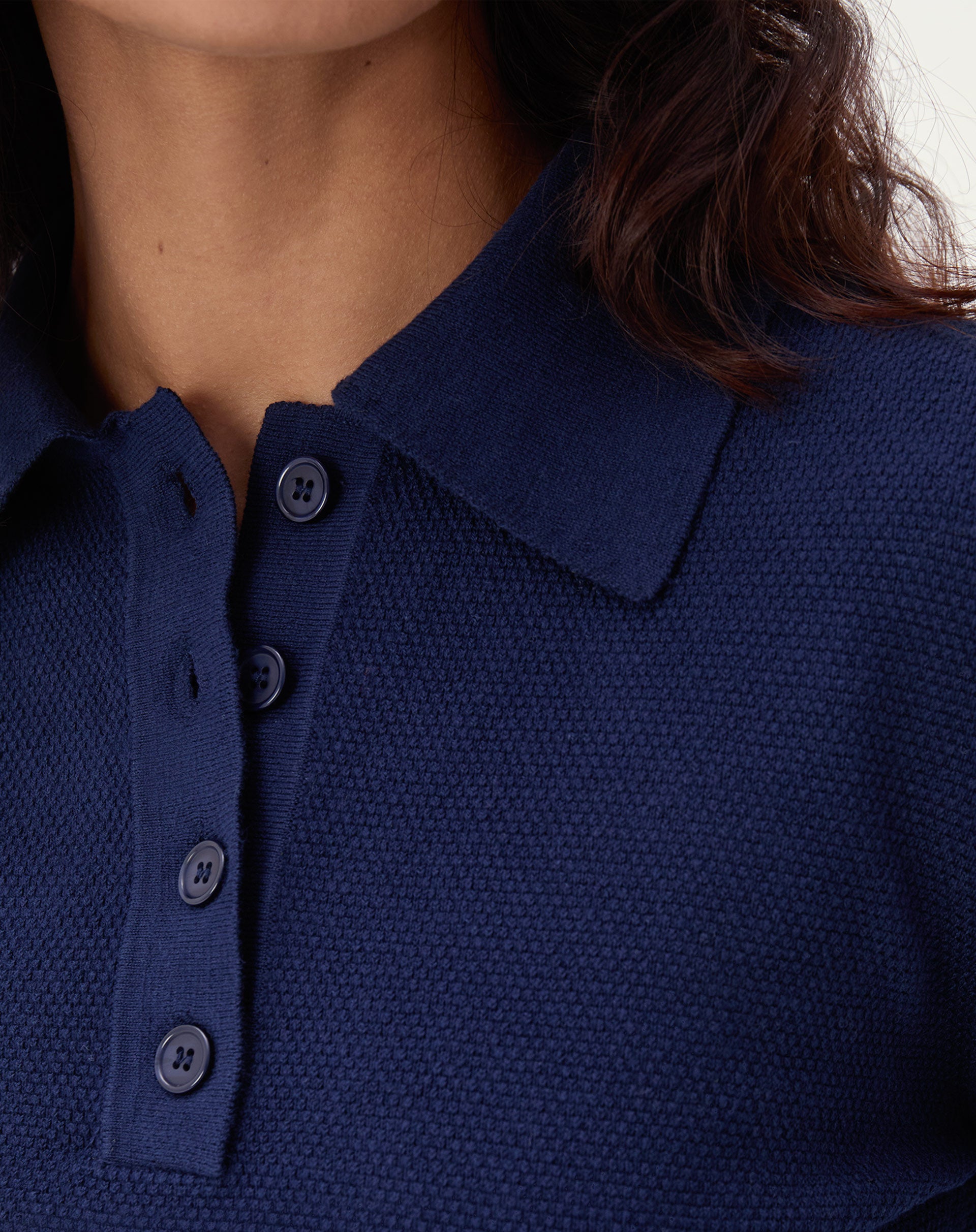 Vista traseira do suéter gola polo de tricô azul marinho mostrando barra canelada e caimento até o quadril, detalhe das costas.