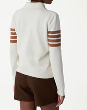 Look completo com suéter gola polo off-white listrado, shorts marrons e sapatos loafers marrons, modelo segurando jaqueta marrom