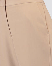 Zoom em detalhe do cós e bolso faca da calça slim alfaiataria bege, evidenciando a qualidade do acabamento.