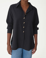 Camisa alongada preta vista frontal em modelo com jeans, colarinho pontudo, abotoamento frontal e fenda lateral visível