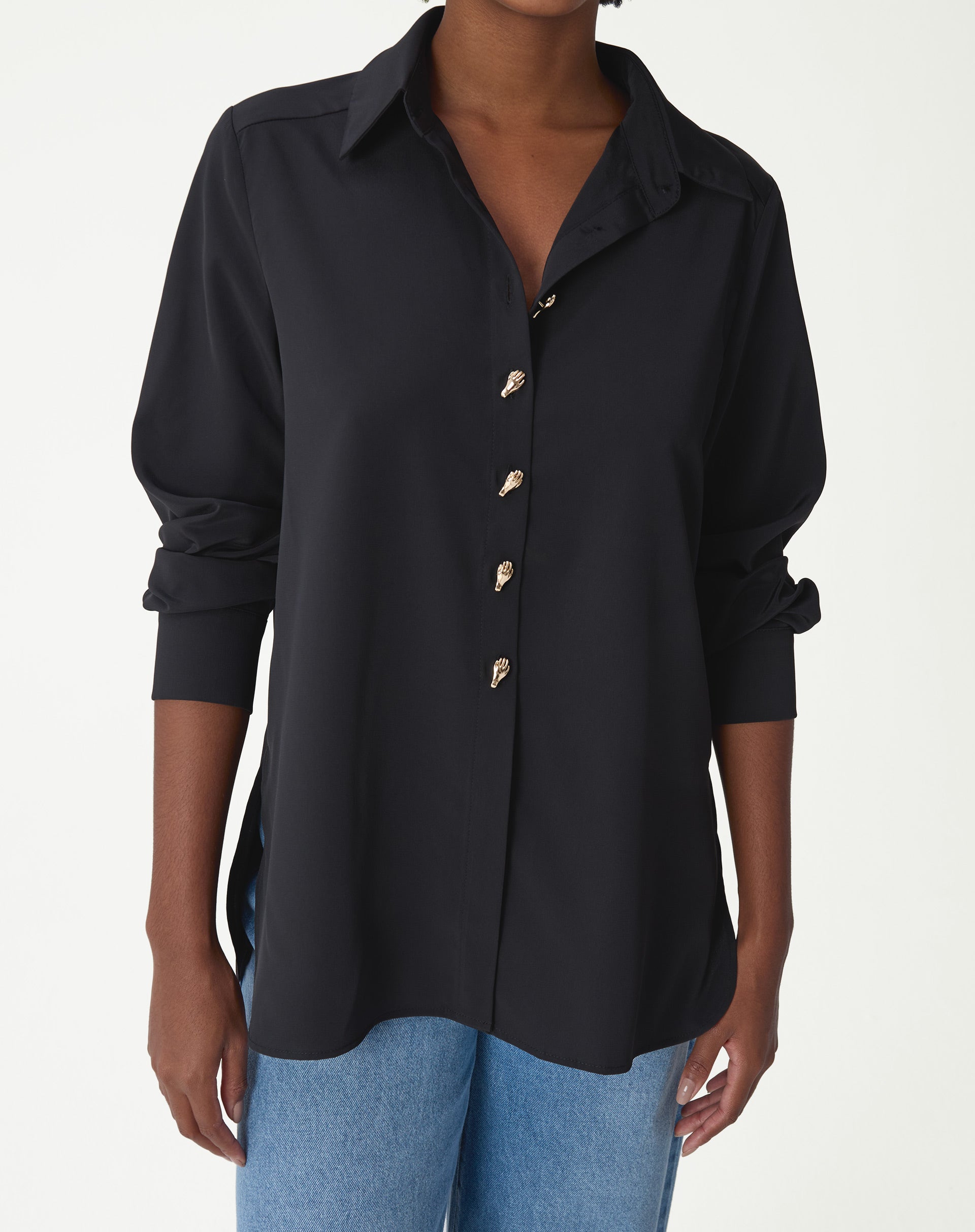 Camisa alongada preta vista frontal em modelo com jeans, colarinho pontudo, abotoamento frontal e fenda lateral visível
