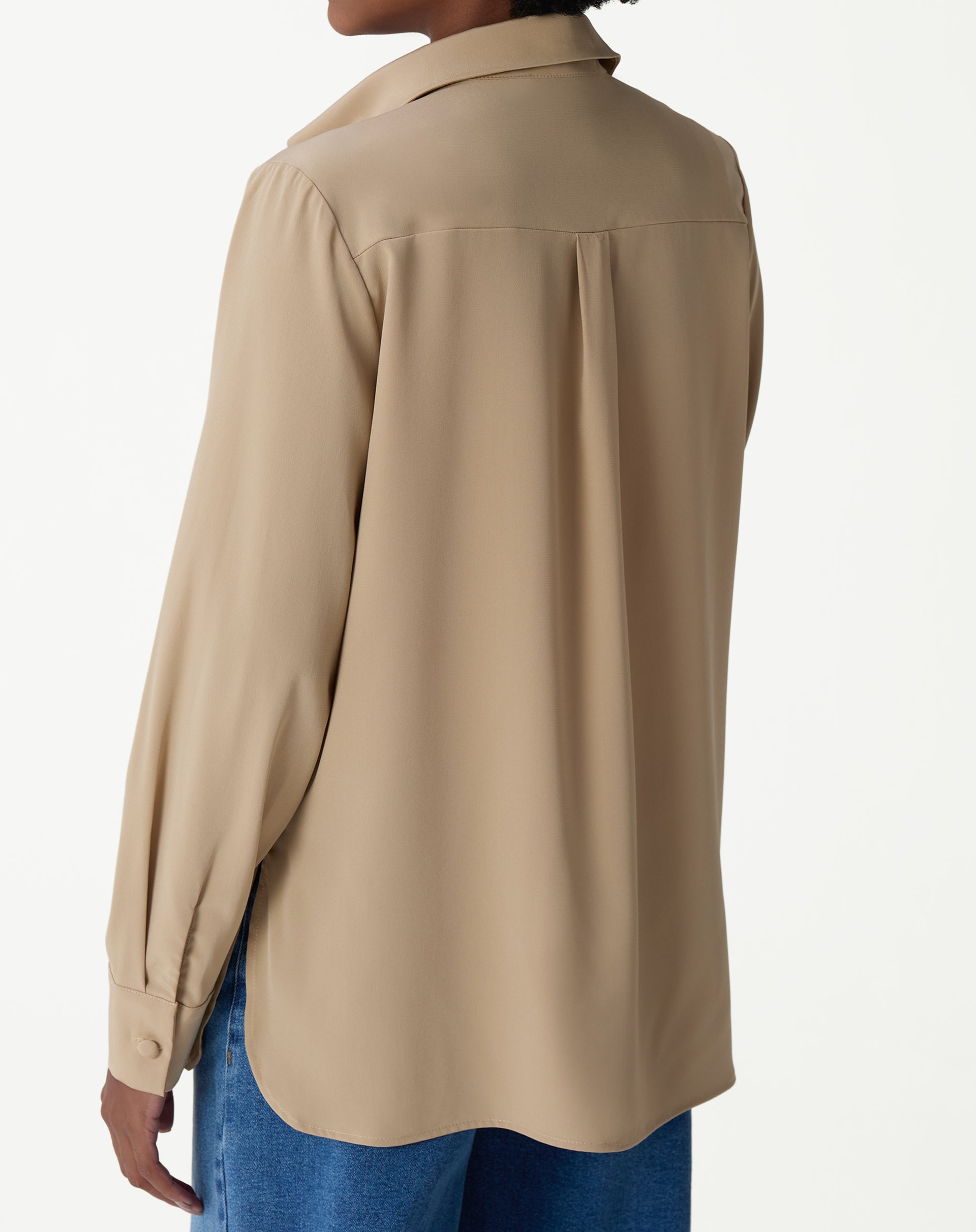 Close-up do colarinho e etiqueta interna (AMARO), mostrando o acabamento do pescoço da camisa bege