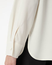 Detalhe da manga e do punho simples da camisa off-white com fenda lateral discreta na lateral da barra