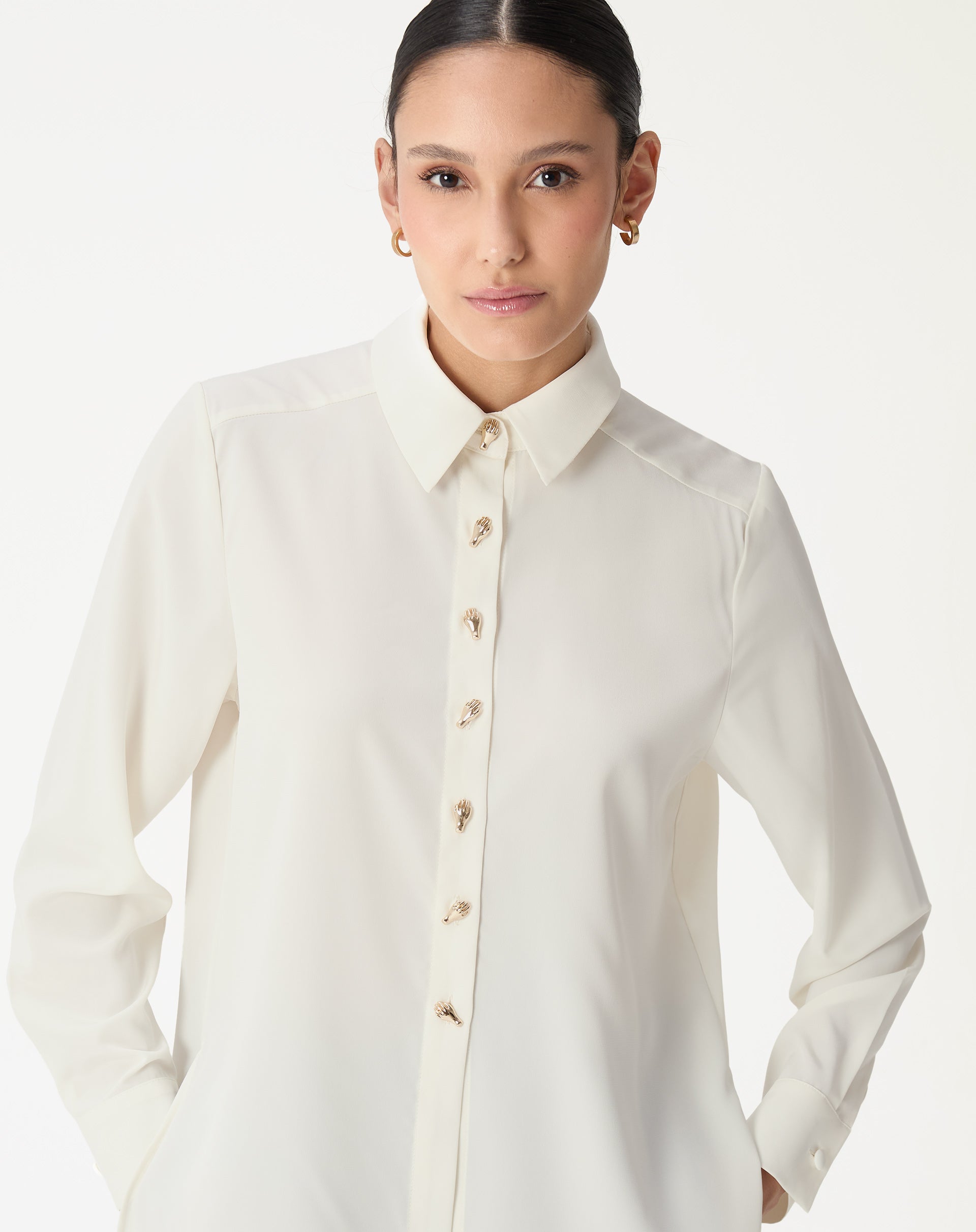 Vista frontal da modelo usando a camisa alongada off-white, destaque para botões dourados e caimento solto