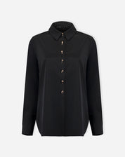 Look completo: modelo com camisa preta alongada por baixo de blazer preto e calça jeans de perna larga, proposta de styling