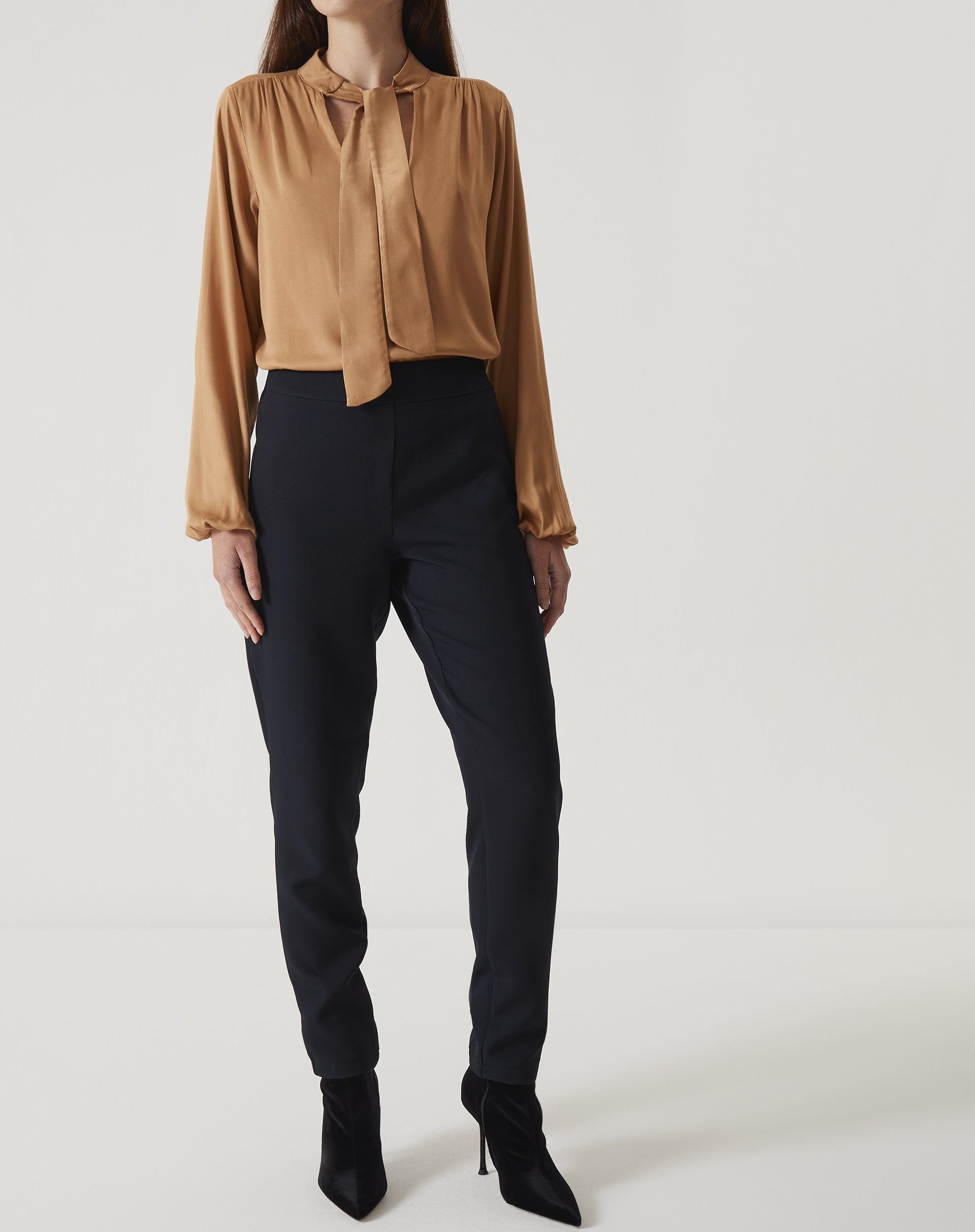 Modelo vestindo calça slim preta de alfaiataria com blusa de seda marrom, vista frontal.