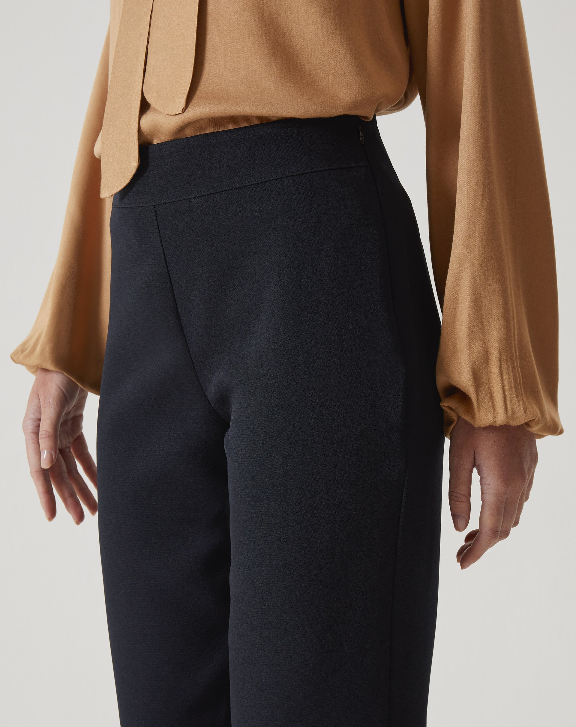 Detalhe do cós alto da calça slim preta de alfaiataria.