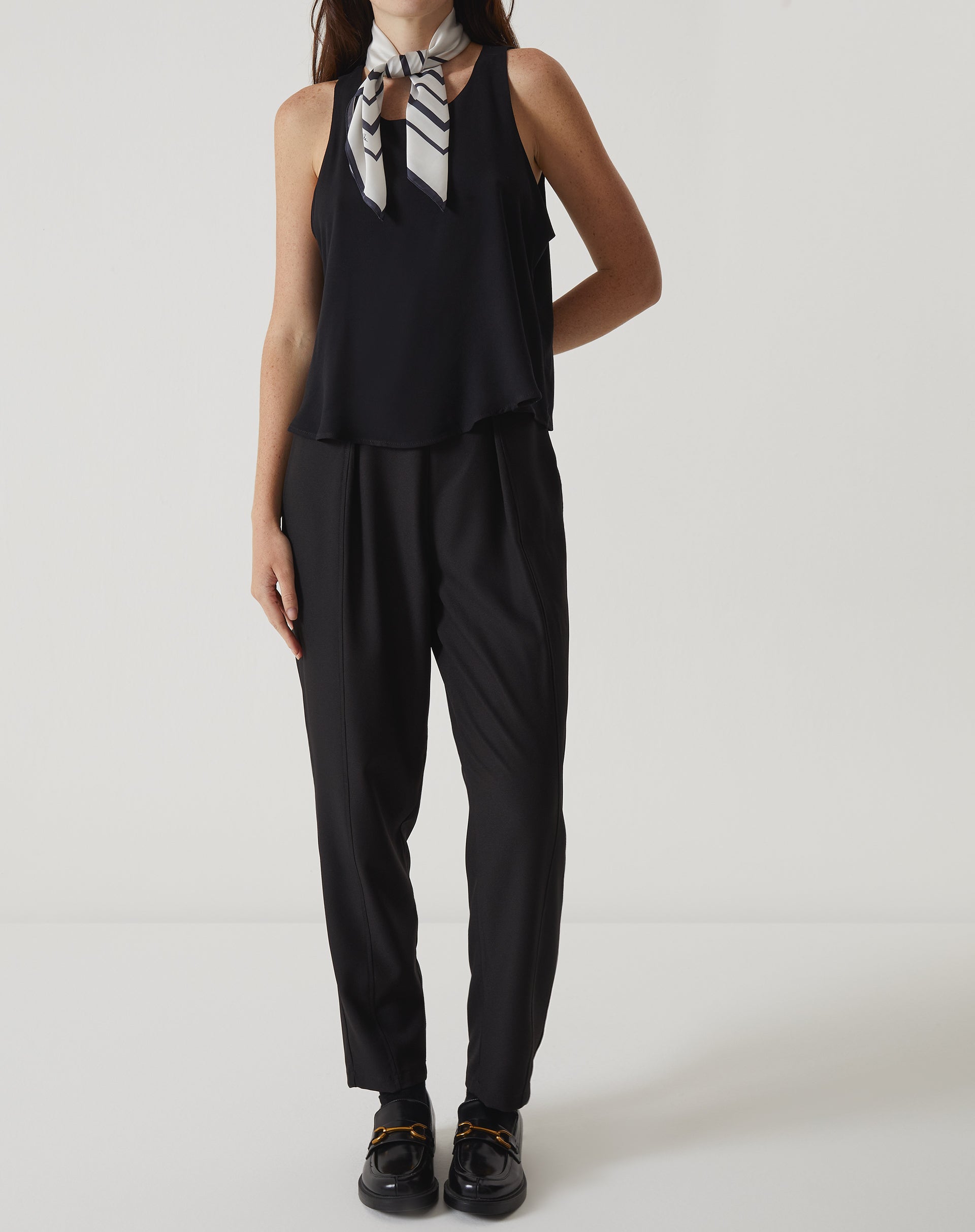 Modelo vestindo a regata preta com babados em um look completo, incluindo acessórios.