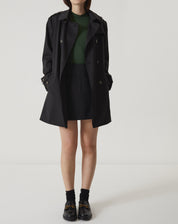 Modelo vestindo regata verde com saia preta e casaco.