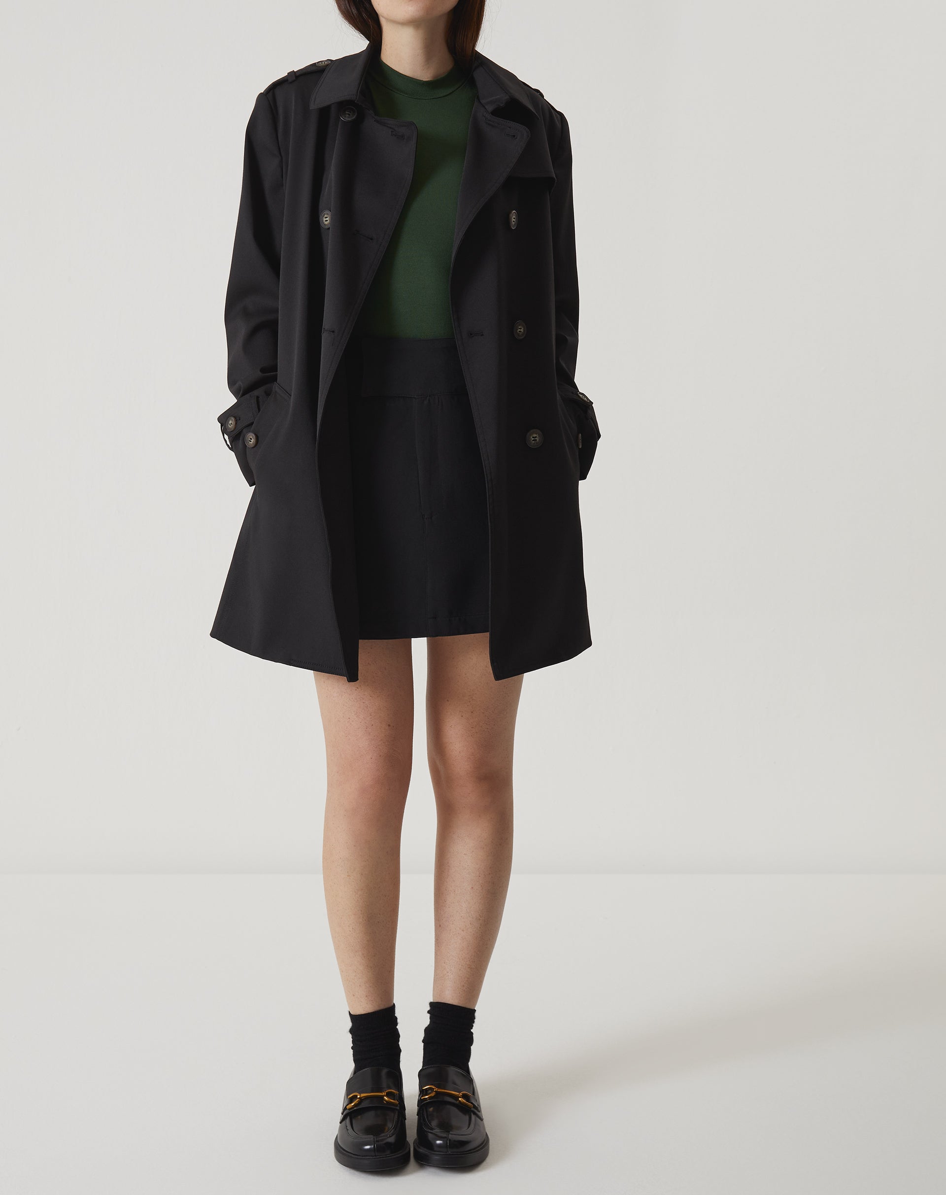 Modelo vestindo regata verde com saia preta e casaco.