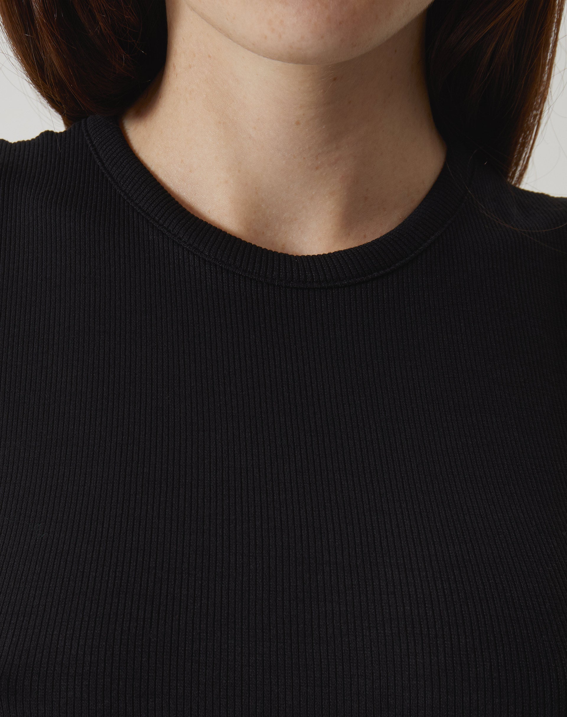 Detalhe do decote gola da regata curta de malha preta, mostrando o tecido e o acabamento.