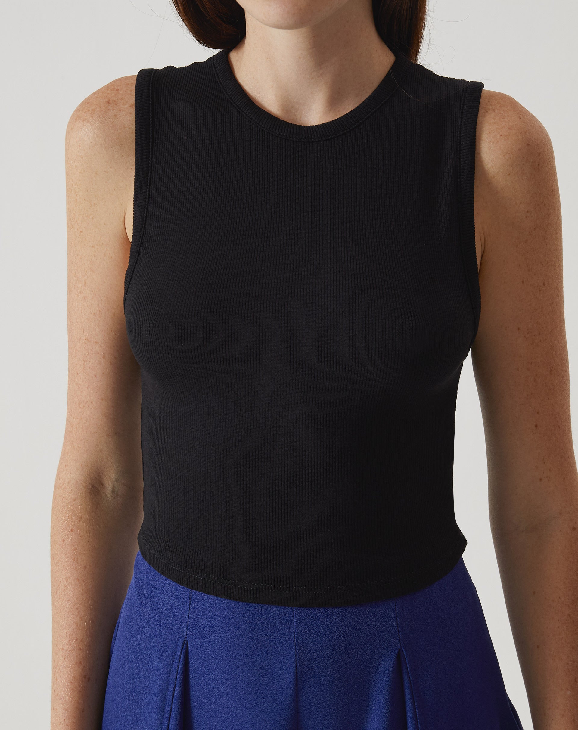 Regata curta de malha preta vista de frente, destacando o design sem alças e o decote gola.