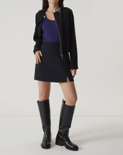 Modelo vestindo saia curta de alfaiataria preta com botas e blusa roxa.