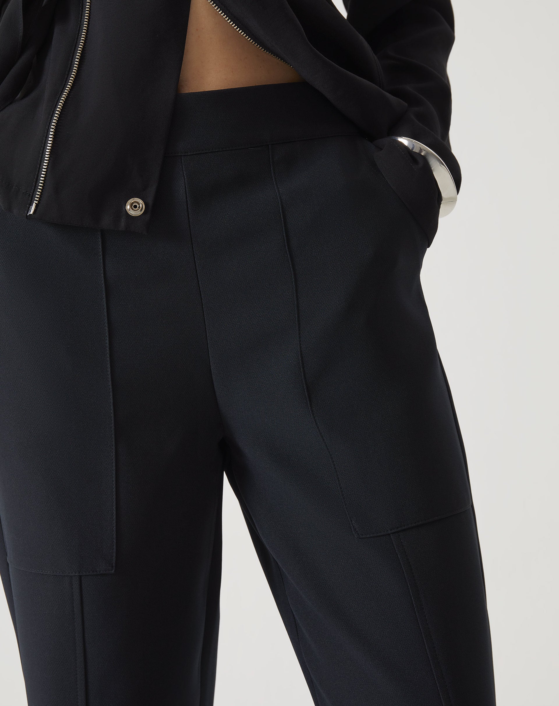 Detalhe do cós e bolsos da calça reta de alfaiataria preta.
