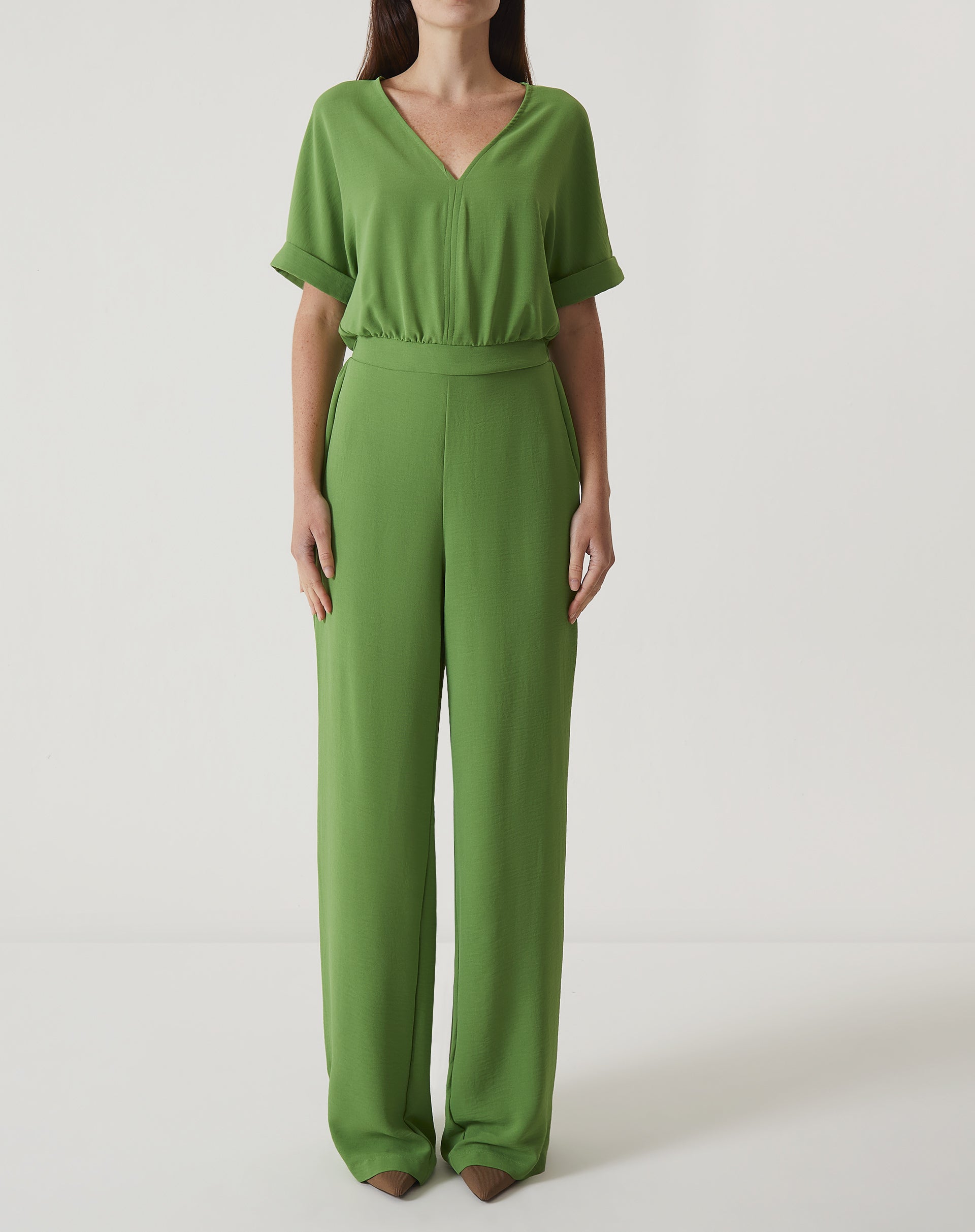 Imagem de um macacão verde com manga curta e decote em V, visto de frente.