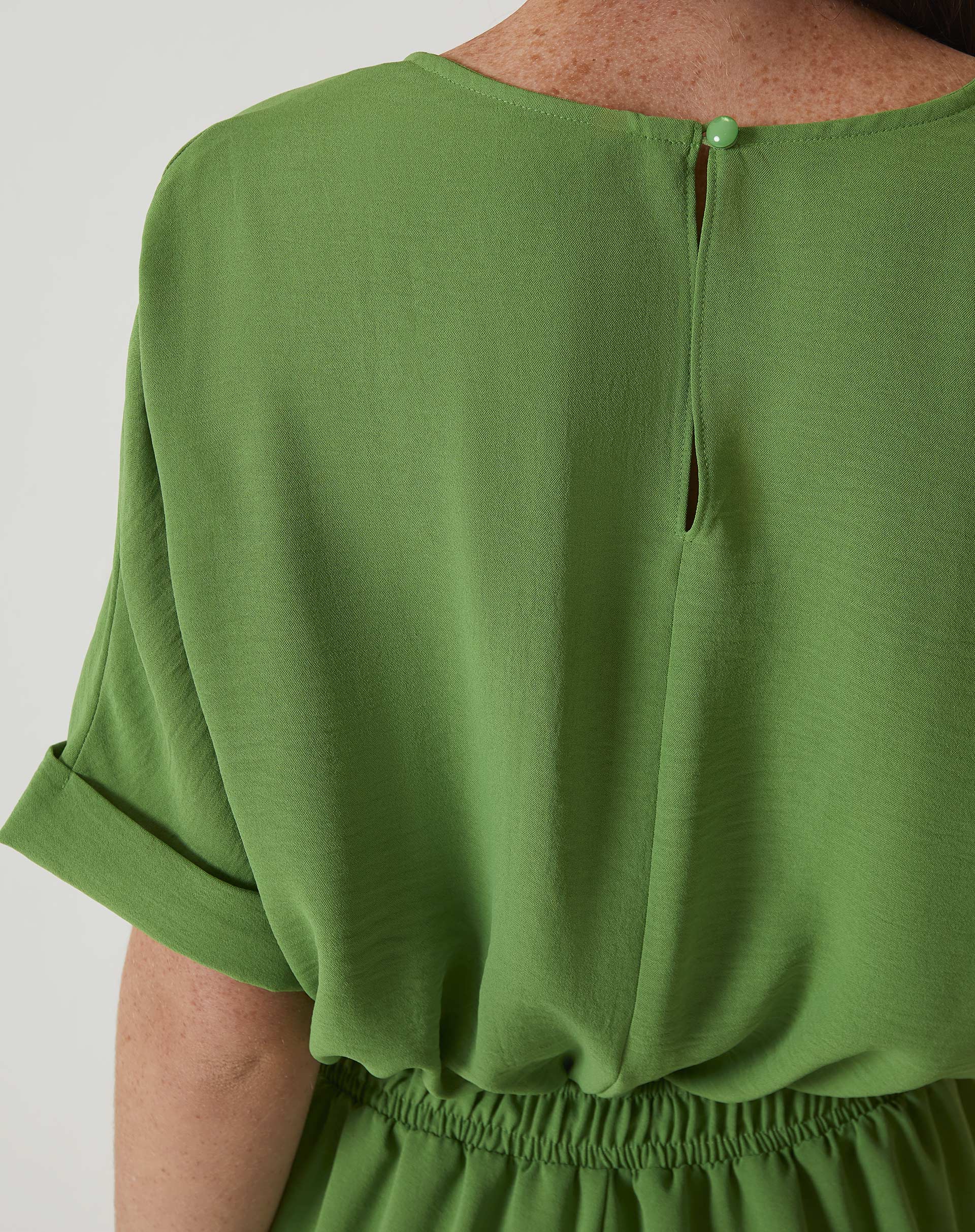 Detalhe da cintura ajustada do macacão verde com elástico.