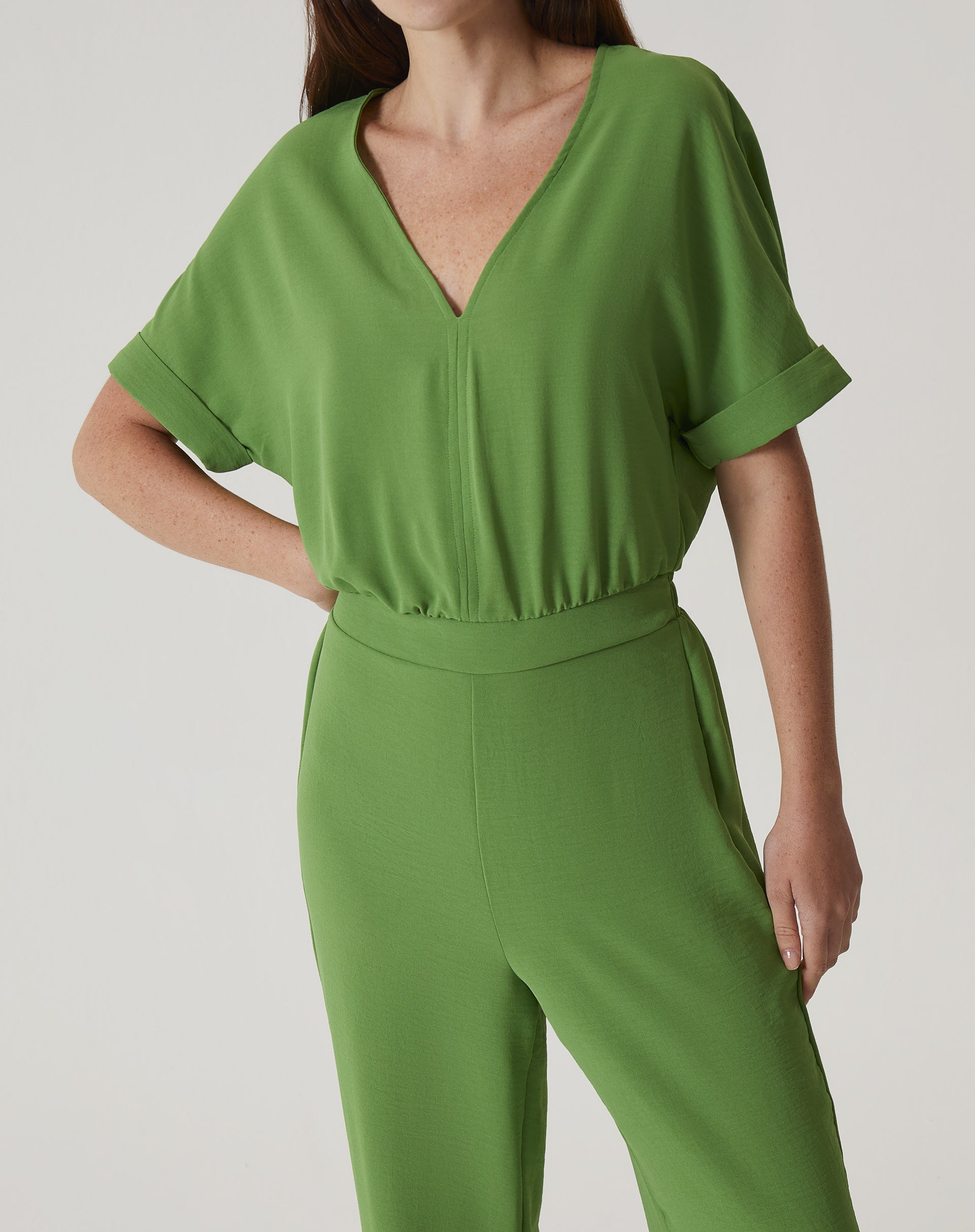 Detalhe do macacão verde mostrando o decote em V e as mangas curtas.