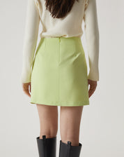 Modelo vestindo saia curta de alfaiataria verde com botas pretas, mostrando o look completo.