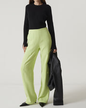 Modelo vestindo calça reta de alfaiataria verde claro com blusa preta e segurando um casaco preto.