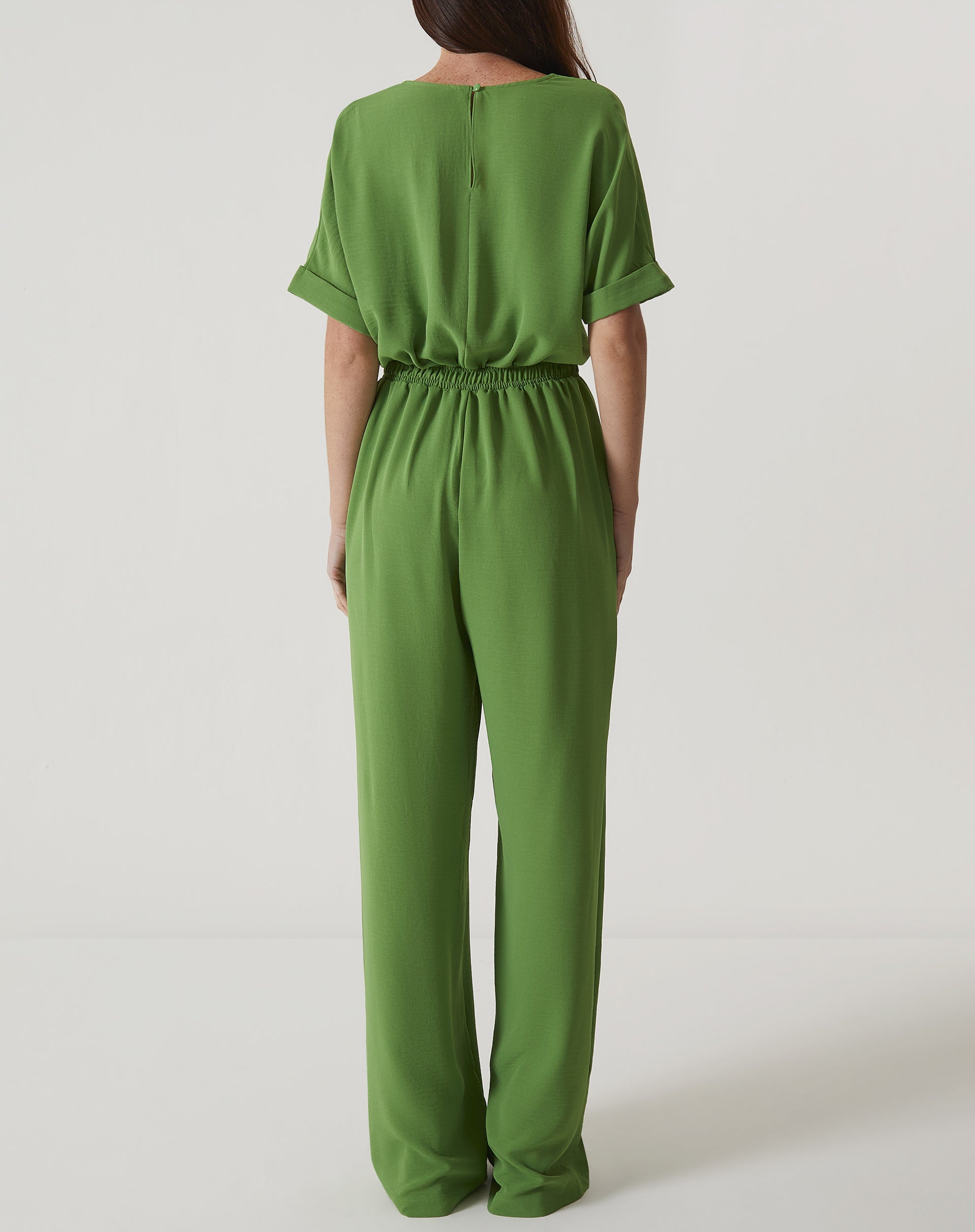 Vista traseira do macacão verde com detalhe de fechamento por botão.