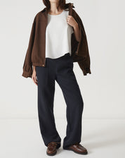 Regata off-white com babados, combinada com calça preta e jaqueta marrom.