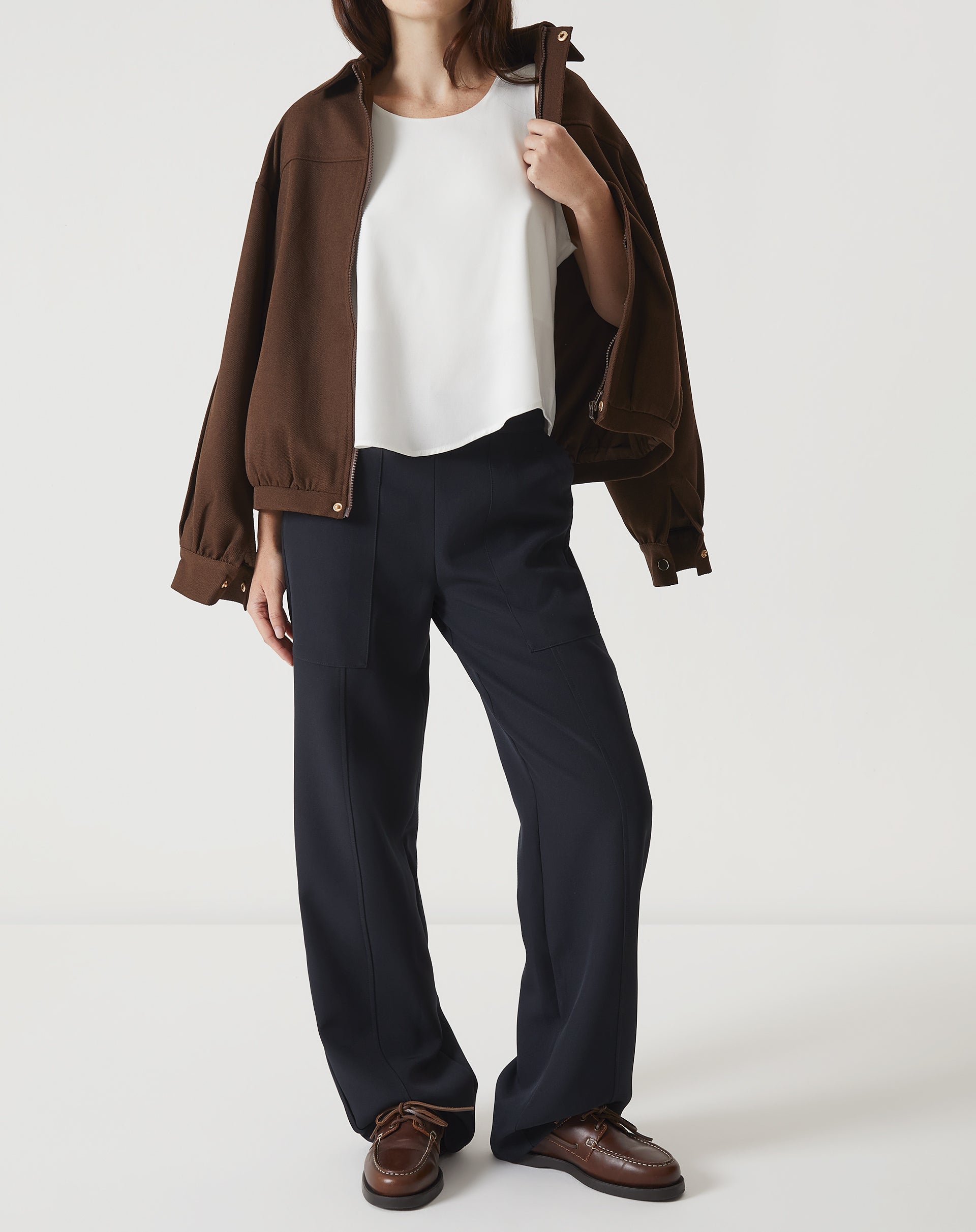 Regata off-white com babados, combinada com calça preta e jaqueta marrom.