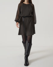 Modelo vestindo um vestido curto verde com mangas longas bufantes, acompanhado de botas pretas.