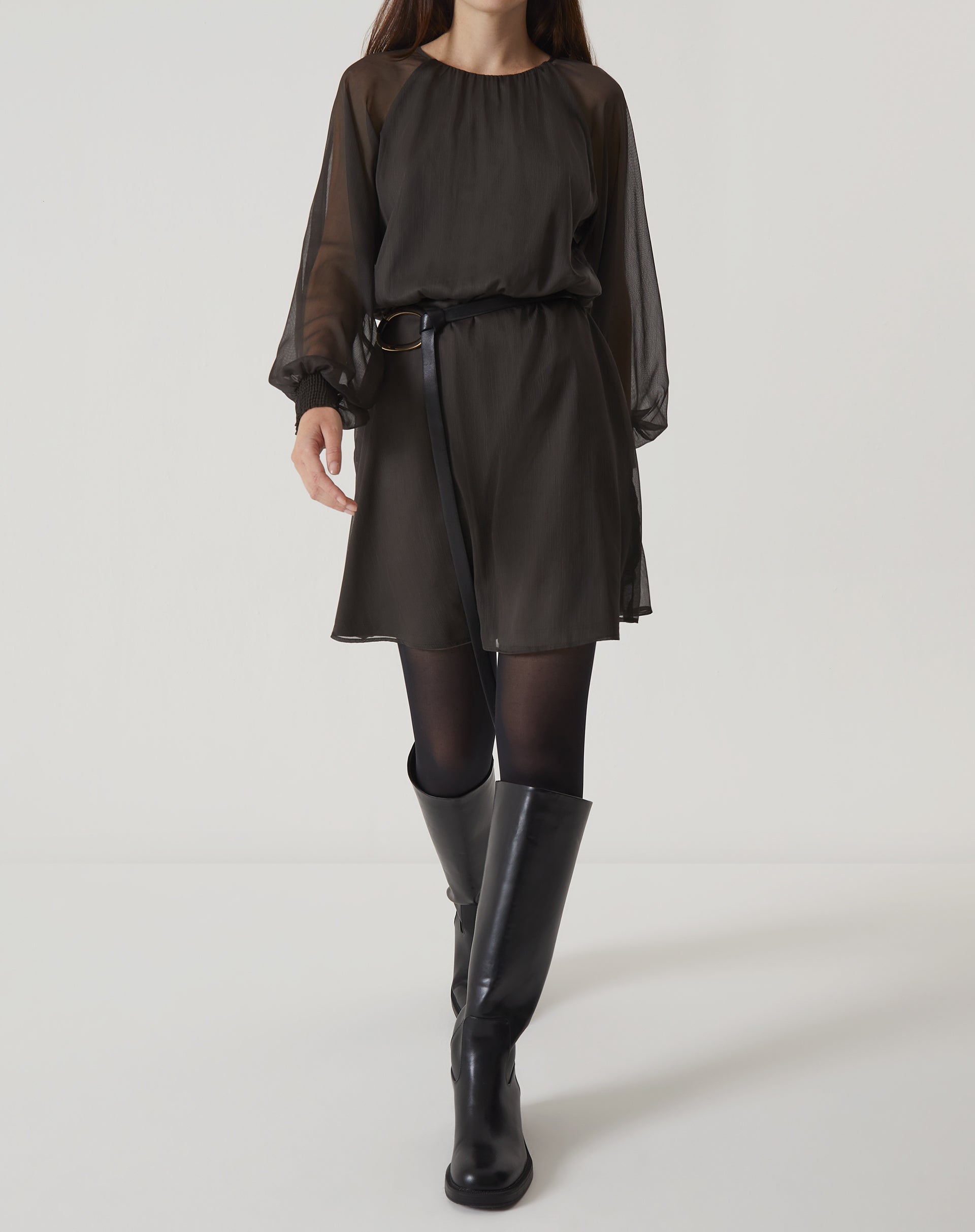 Modelo vestindo um vestido curto verde com mangas longas bufantes, acompanhado de botas pretas.